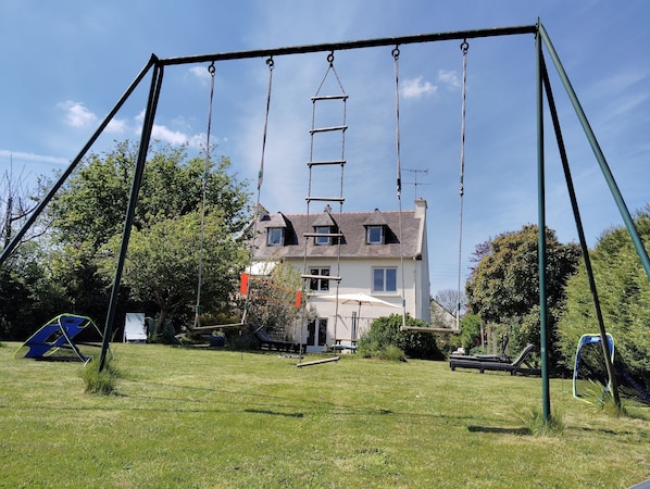 Eine Schaukel auf einer grünen Wiese, im Hintergrund ein Haus.
