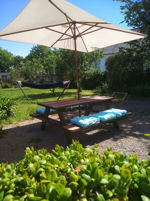 Ein Holztisch mit blauen Kissen, eine Hängematte und ein großer Sonnenschirm in einem Garten.