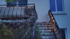Une maison à deux étages avec un escalier menant à l’étage supérieur, un balcon décoré de guirlandes lumineuses et une fenêtre offrant une vue sur le ciel.