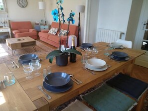 Ein Essbereich mit Holztisch, gedeckt für eine Mahlzeit, umgeben von einem Wohnzimmer mit Sofa und Zimmerpflanzen.
