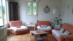 Un salon avec un plancher en bois, un ensemble de canapés roses, une petite table et une plante en pot au premier plan.