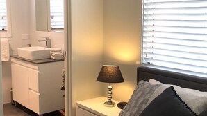 Ett sovrum med en säng, ett nattduksbord, en lampa och utsikt över ett badrum med handfat och spegel.