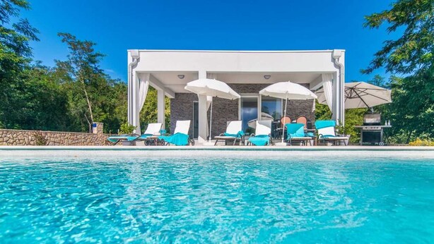A pool with clear water, surrounded by lounge chairs and umbrellas, with a building in the background. - Villa Sofia (Santalezi)