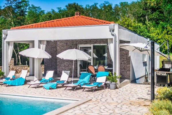 Un espace aménagé au bord de la piscine, avec des chaises longues, des parasols et un barbecue.