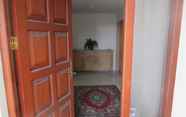 Un couloir avec une porte en bois, un tapis à motifs et un meuble orné d’une plante.