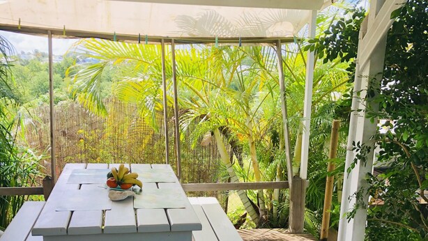 A covered outdoor area with a wooden deck and a white picnic table with benches. - Bungalow La Colline aux Moulins (Sainte-Anne)