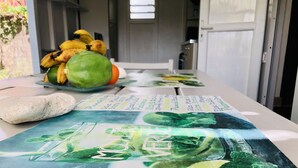A table with a menu, a bunch of bananas, a lime, and a green fruit. - Bungalow La Colline aux Moulins (Sainte-Anne)