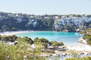 A coastal landscape with a clear turquoise bay, white cliffs, and a beach area with boats and umbrellas.