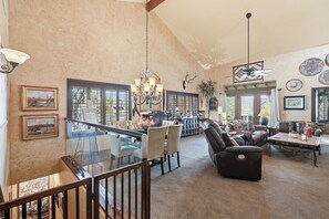 A spacious living area with a high ceiling, a glass staircase, and a large dining table.