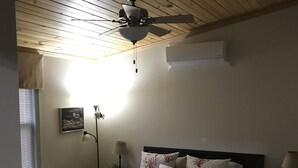 Quarto com cama, ventoinha no teto, mesa de cabeceira com abajur e ar condicionado.