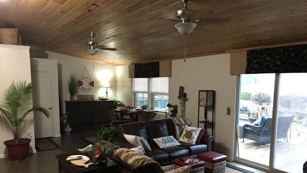 Uma sala de estar aconchegante com um sofá de couro escuro, uma mesa de centro e uma área de jantar com mesa e cadeiras. Há uma grande janela que oferece vista para o exterior.
