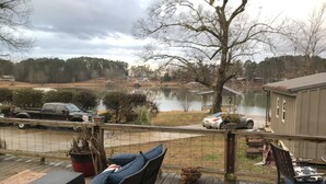 Um deck com móveis de exterior, vista para um lago e um píer com um barco.
