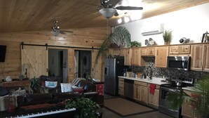 Um interior acolhedor estilo cabana com sala de estar que inclui um piano, um sofá e uma lareira. A cozinha possui armários de madeira, um micro-ondas e um fogão.