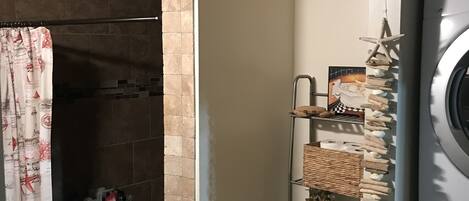 Un bagno con doccia, WC e lavabo. È presente una lavatrice e uno scaffale con articoli da toilette.