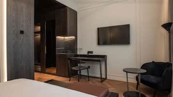 Et moderne hotelværelse med seng, skrivebord med stol, et lille bord og et tv ophængt på væggen.
