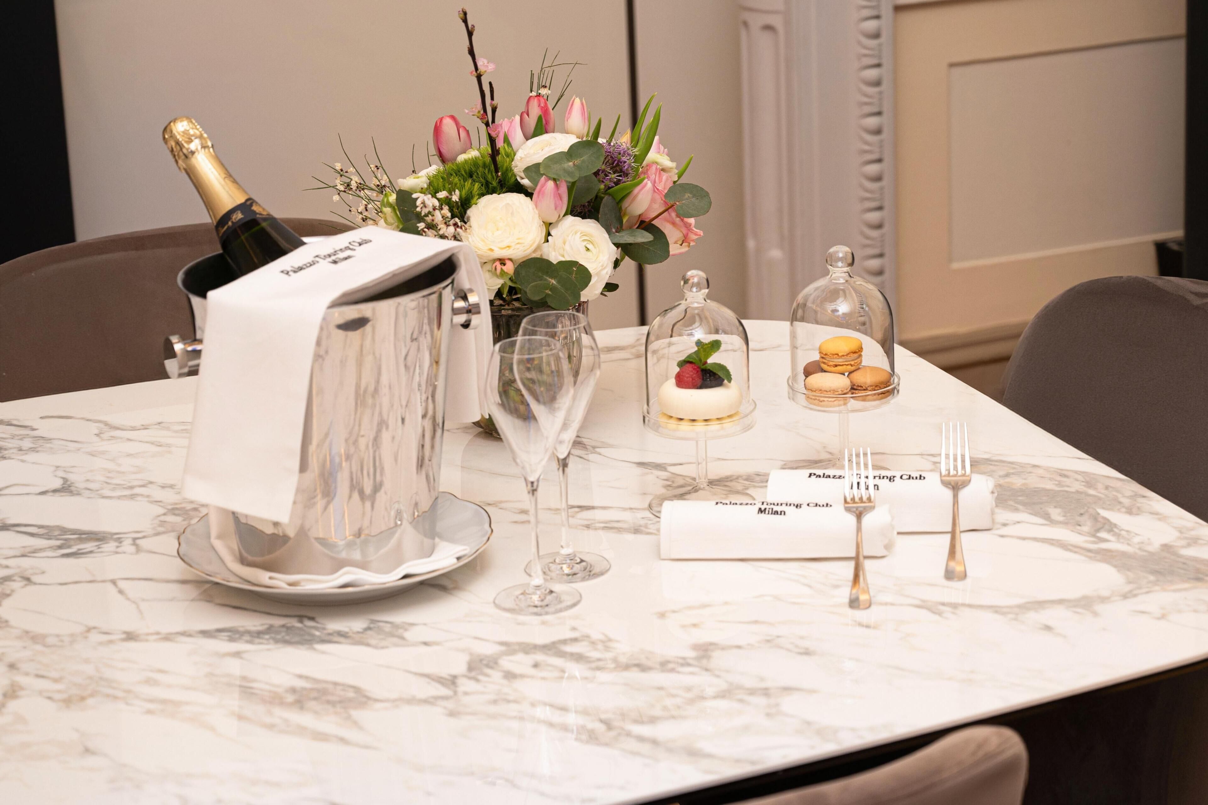 A table set with a bottle of champagne, a vase of flowers, a dessert, and cutlery.