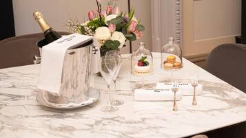 A table set with a bottle of champagne, a vase of flowers, a dessert, and cutlery.