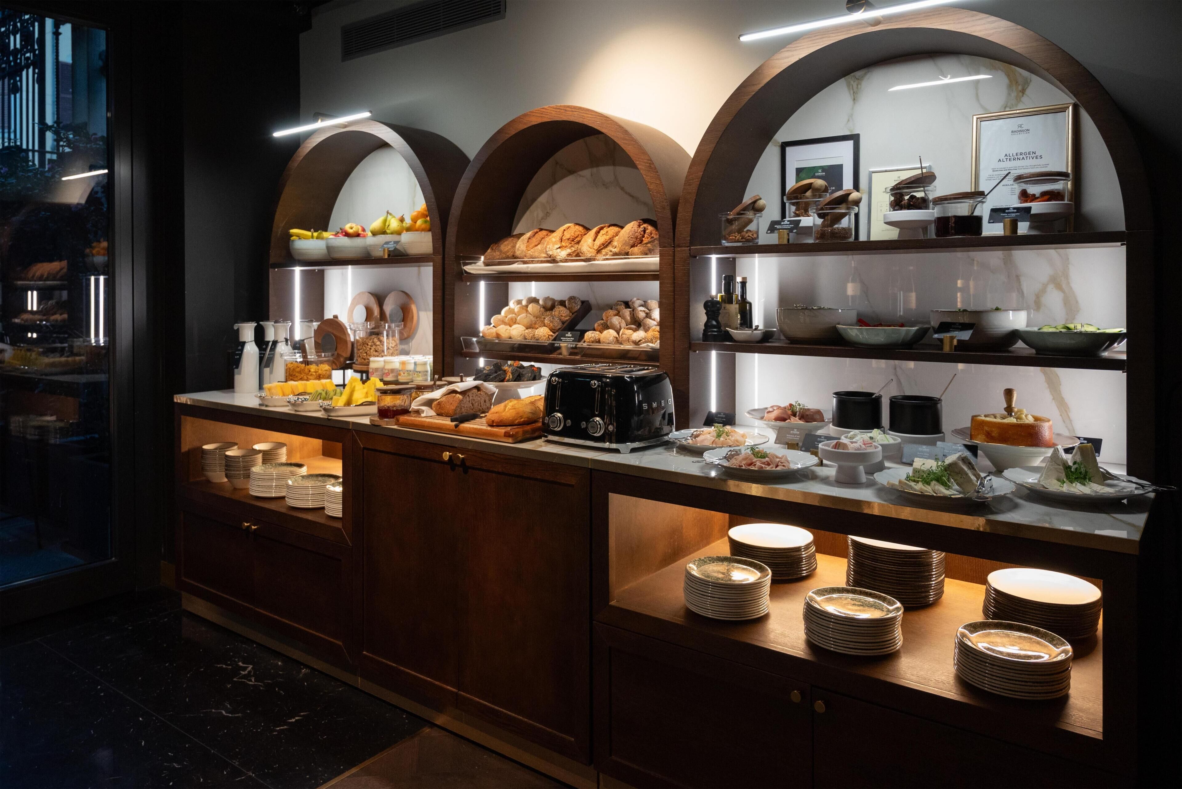 Montaje de bufé con diversas opciones de comida, una máquina de café y platos apilados ordenadamente.