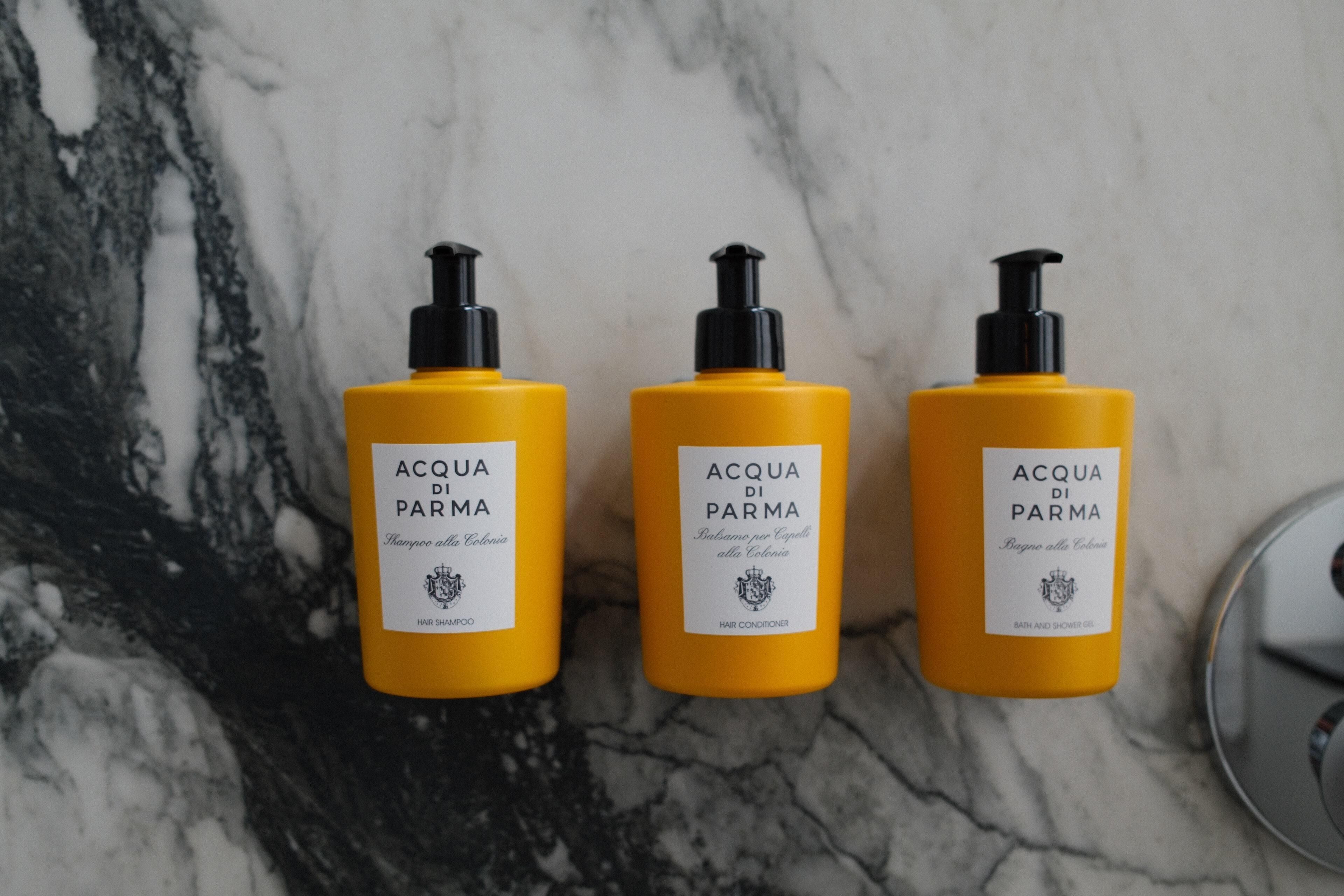 Three bottles of Acqua di Parma hair products on a marble surface.
