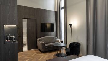 Une chambre d’hôtel moderne avec un grand lit, un canapé, une petite table, un téléviseur fixé au mur et une fenêtre avec des rideaux.