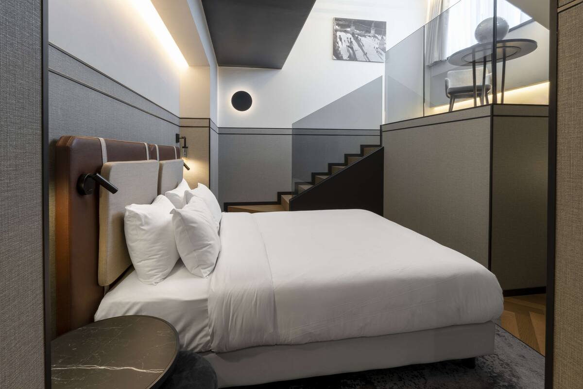 A modern bedroom with a large bed, a round side table, and a staircase leading to an upper level.