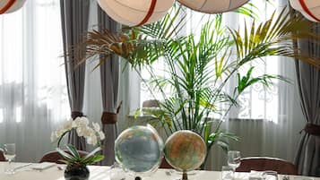 A dining table set with a globe, orchids, and a vase of green plants.