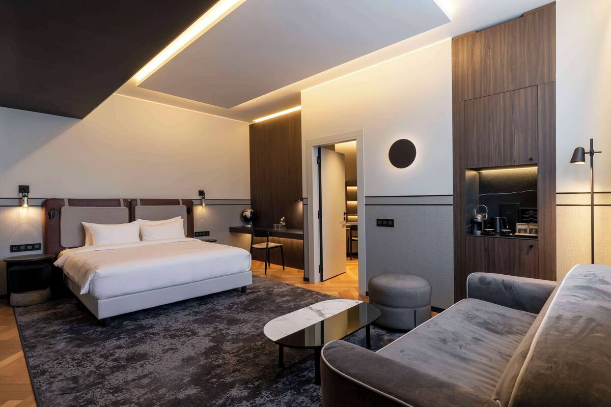 A modern bedroom with a large bed, a sofa, a small table, and a built-in TV.