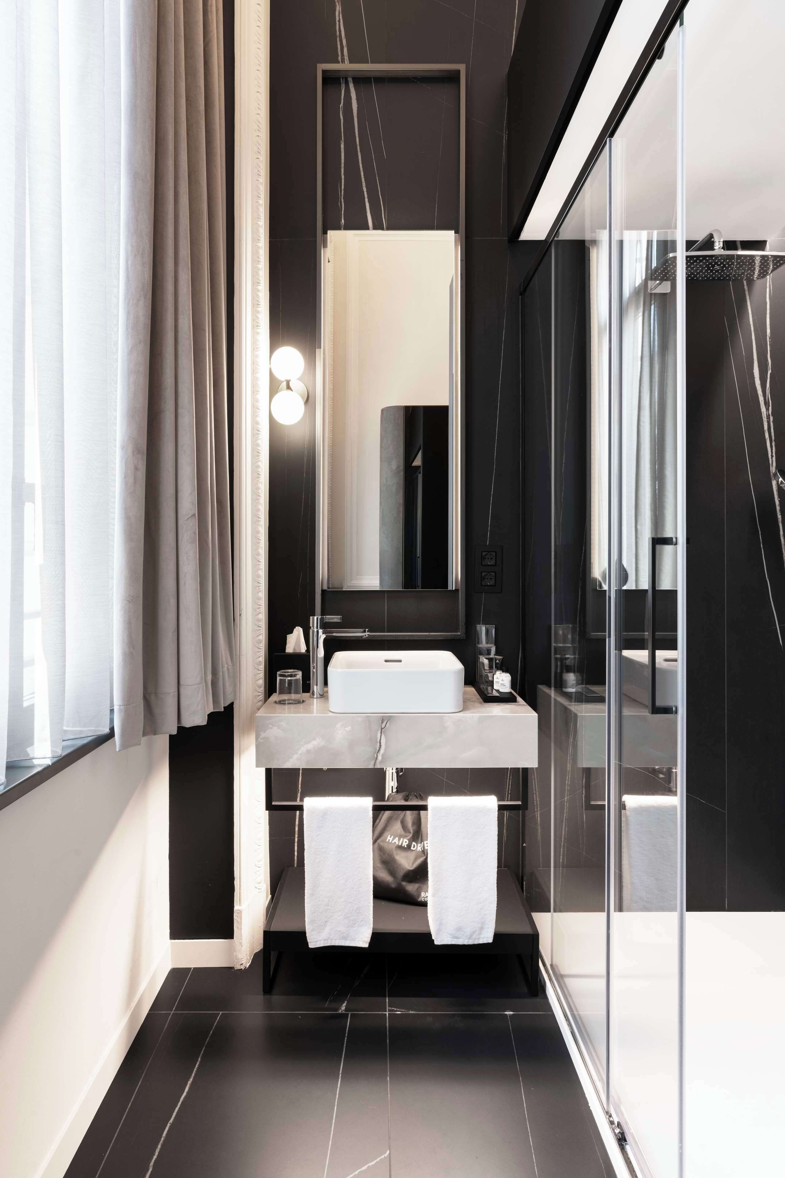 A modern bathroom with a large mirror, white sink, and a glass shower enclosure.