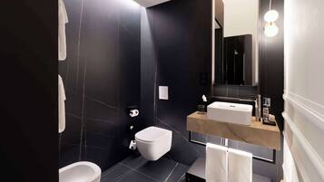 A modern bathroom with a black marble wall, a white toilet, a bathtub, and a vanity with a mirror and sink.