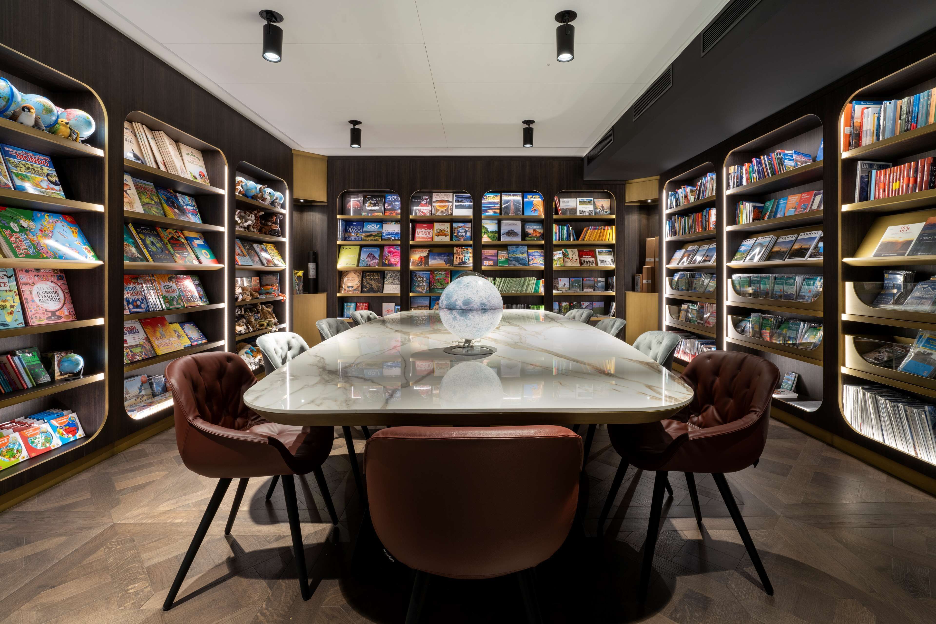 Una biblioteca con una mesa de cristal central rodeada de sillones de cuero, todo ello enmarcado por estanterías llenas de libros y objetos decorativos.
