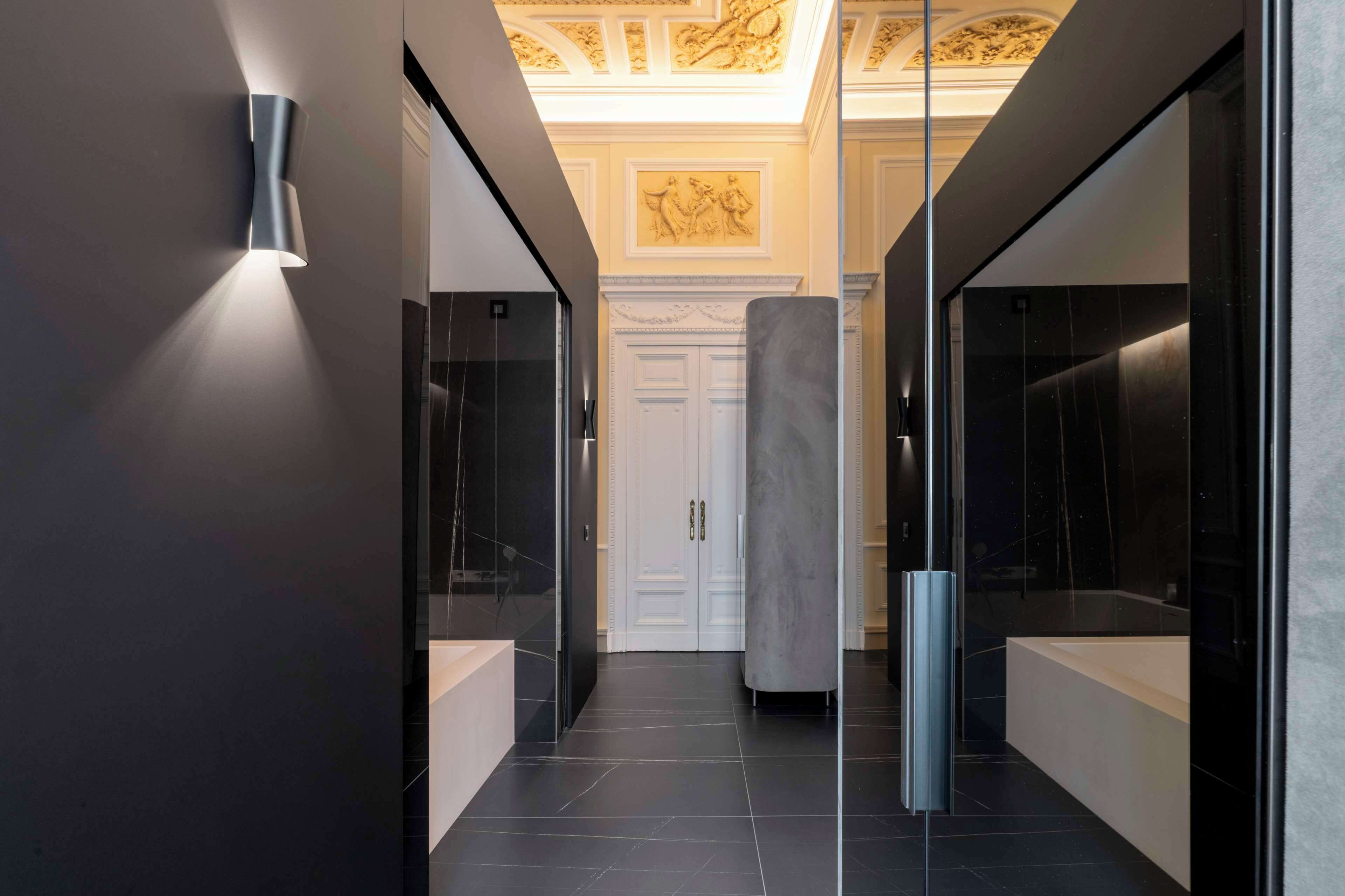 A modern hallway with a glass door, a marble column, and a light fixture on the wall.