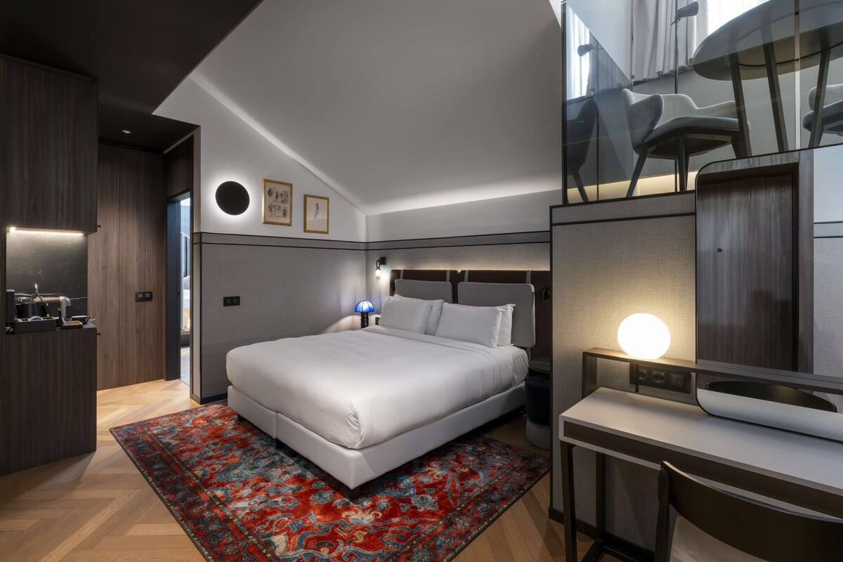 A modern hotel room with a large bed, a desk, and a small seating area.