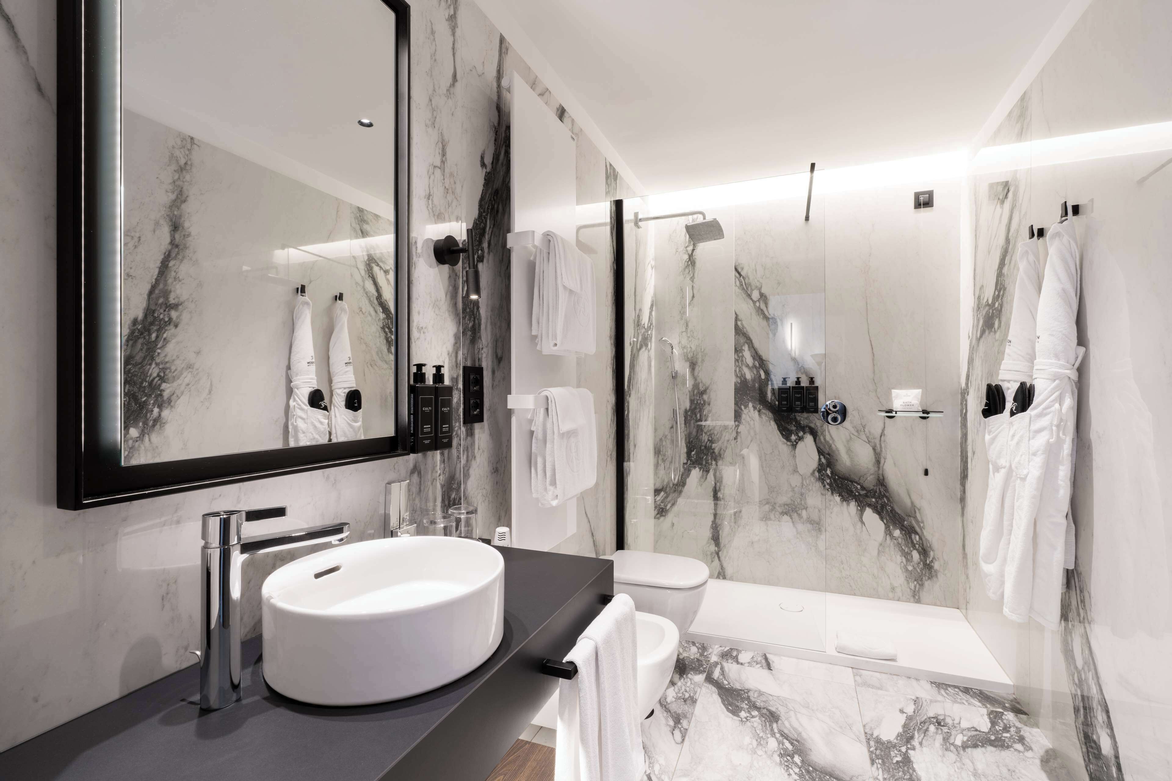 A modern bathroom with a large mirror, a round sink, a toilet, and a shower area.