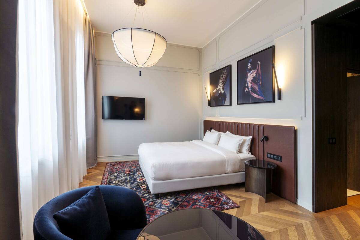 A modern hotel room with a large bed, a flat-screen TV, a desk, and a chair.