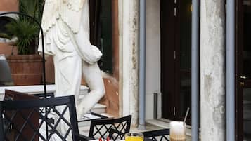 A table set outdoors with a statue of a figure, a potted plant, and a meal including a bowl of salad, a glass of orange juice, and a coffee drink.