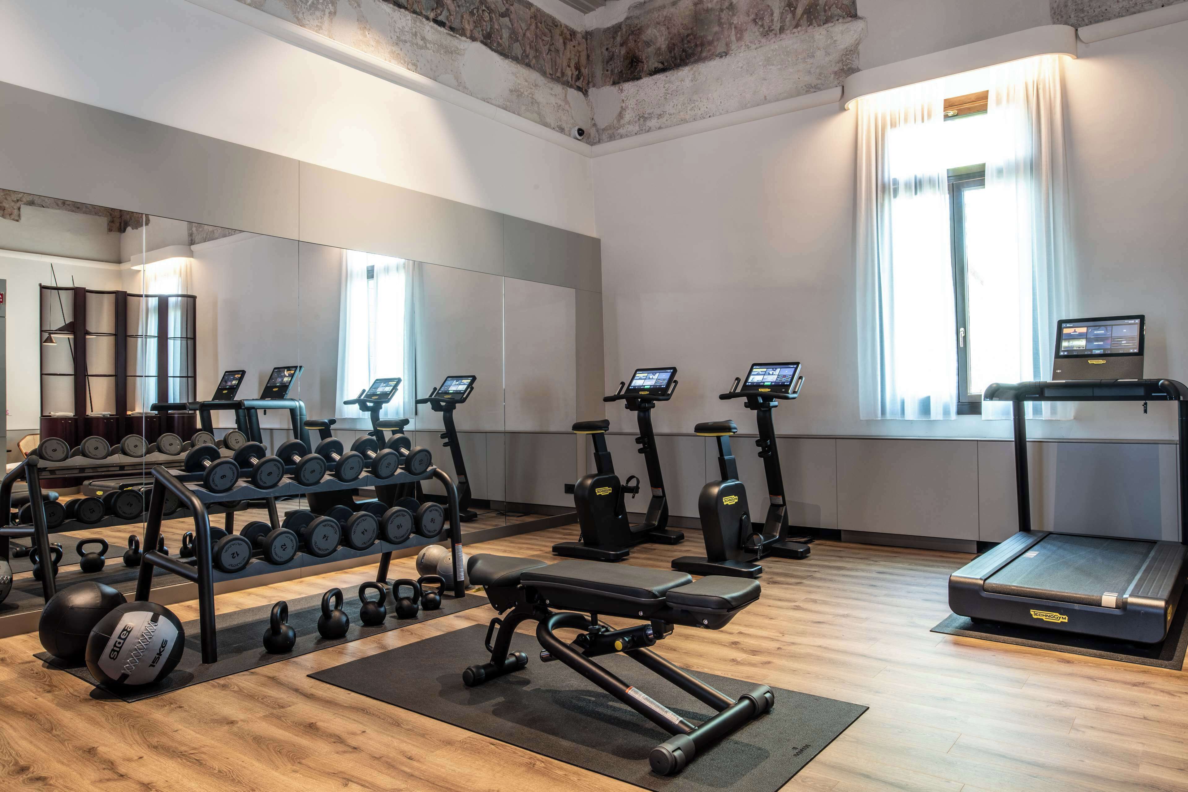 Un gimnasio con varios equipos de ejercicio, como mancuernas, kettelbells, una prensa de banca y cintas de correr.