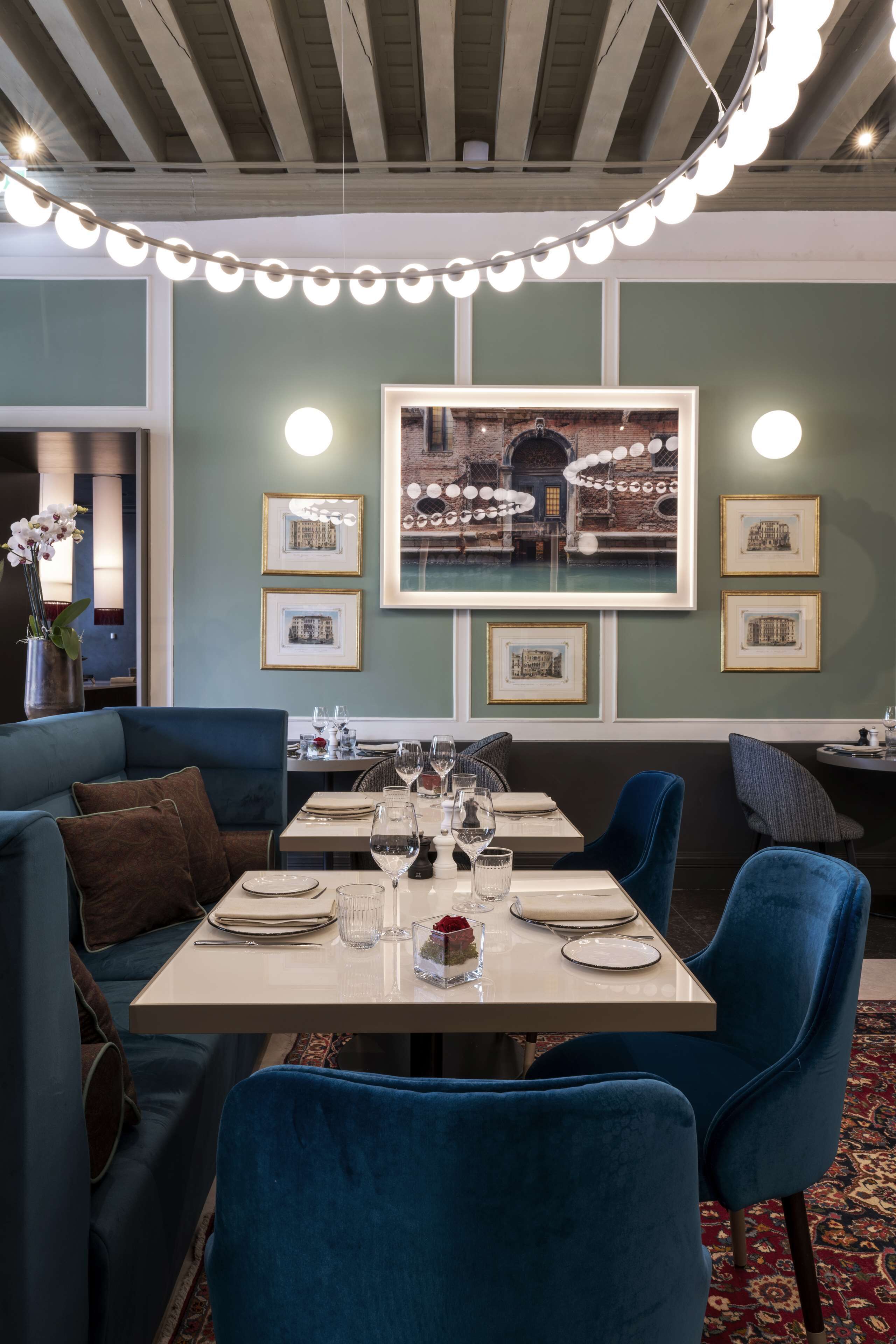 A dining area with a table set for two, a blue sofa, and framed pictures on the wall.