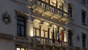 A historic building with ornate balconies, multiple flags, and a well-lit entrance. - Radisson Collection Hotel, Palazzo Nani Venice (Venice)