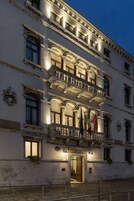 Um edifício histórico com varandas ornamentadas, várias bandeiras e uma entrada bem iluminada.