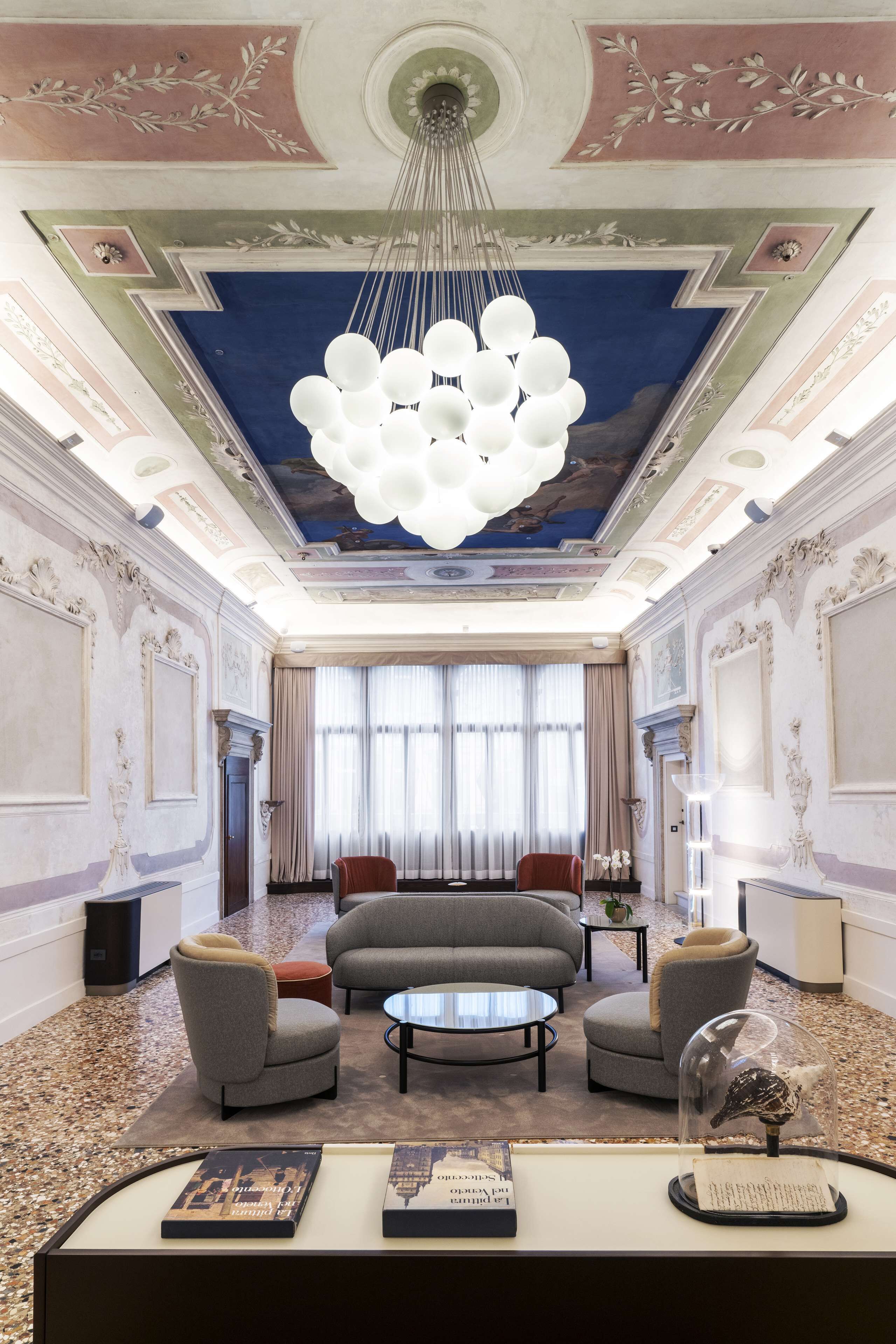 A luxurious hotel lobby with a grand chandelier, elegant furniture, and a decorative ceiling.