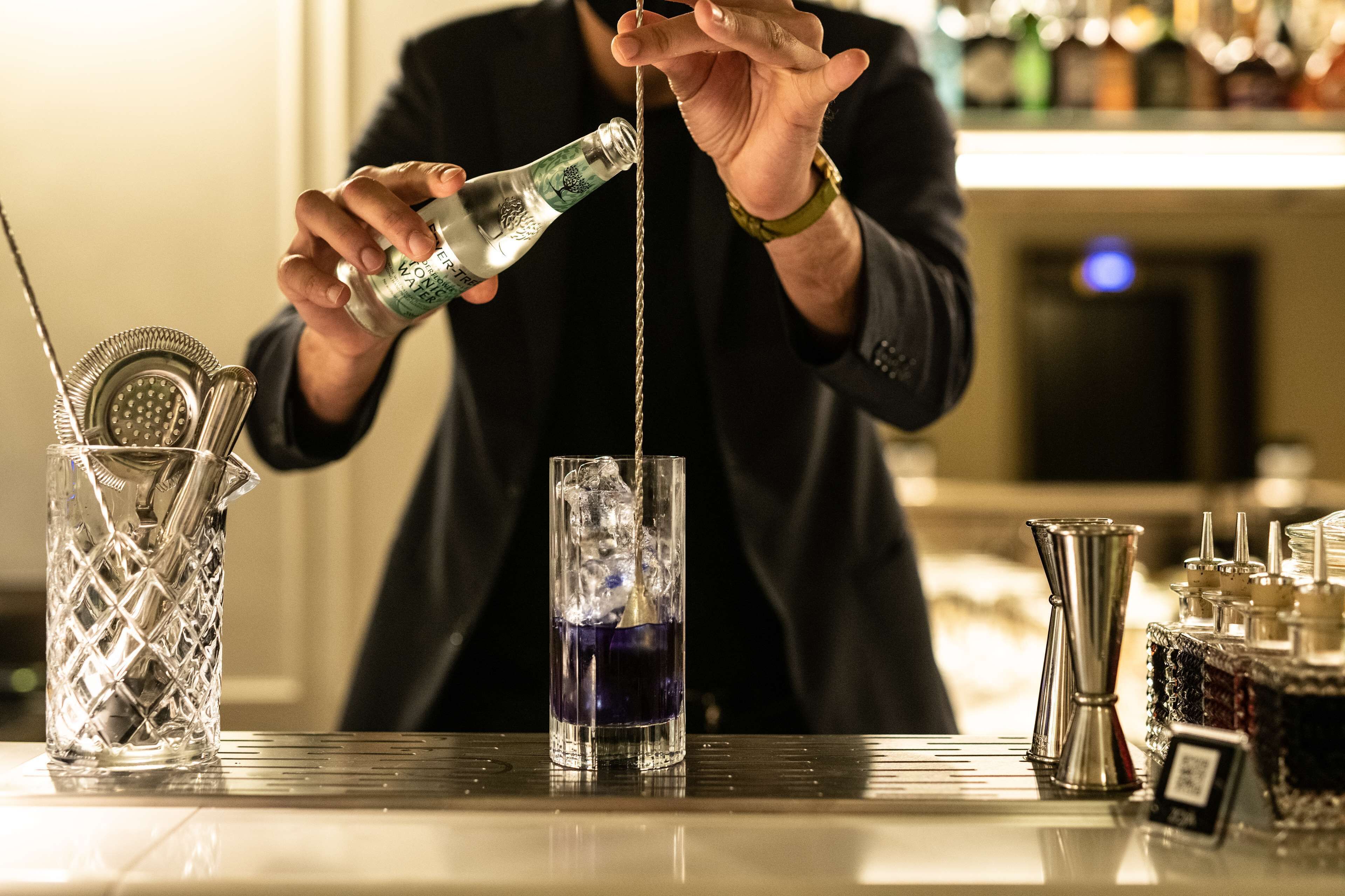 A bartender pouring a drink into a tall glass.