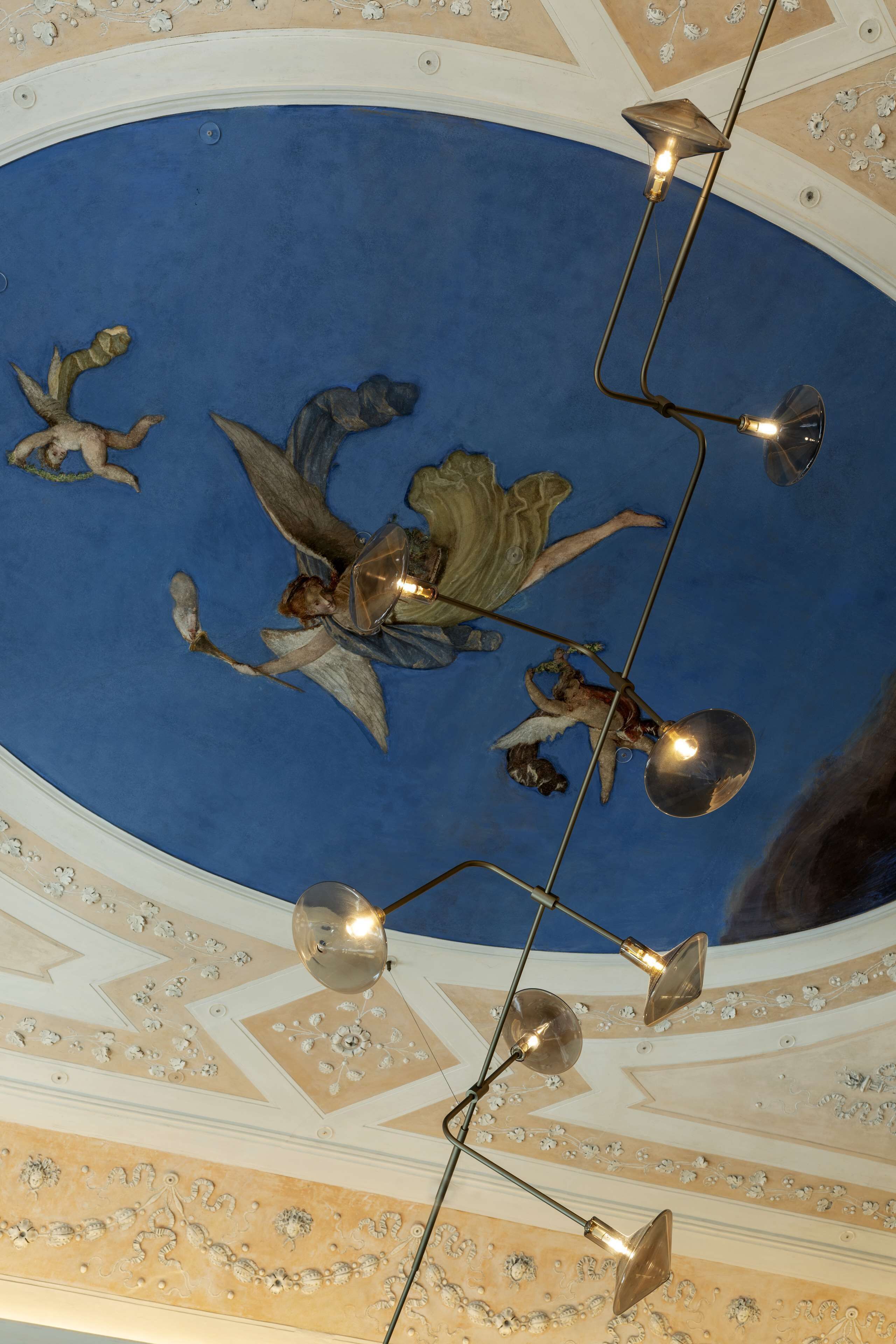 Teto com área central azul e anjos decorativos, com luminária moderna e várias lâmpadas.