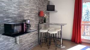 Una cocina moderna con microondas, cafetera y televisor de pantalla plana montado en la pared. Hay tres taburetes de bar con asientos blancos y mullidos.