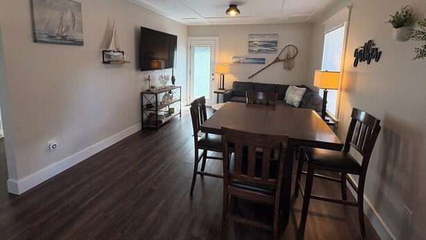 A dining area with a wooden table and chairs, a television mounted on the wall, and a ceiling light fixture.