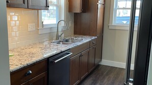 A kitchen with wooden cabinets, a granite countertop, a dishwasher, and a window with a view.