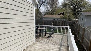 A wooden deck with a white railing, a table, and two chairs.