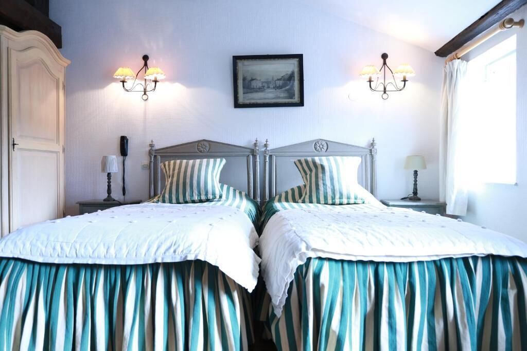A double bed with striped bedding, two bedside tables with lamps, a framed picture on the wall, and a window with curtains.
