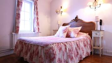 Un dormitorio con una colcha estampada con motivos florales, cabecera de madera, lámparas de noche y un radiador.