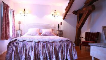 A bedroom with a large bed, two bedside lamps, a chair, and a wooden beam structure.