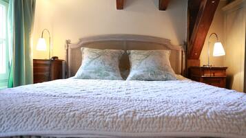 A neatly made bed with a patterned bedspread and two matching pillows, flanked by bedside tables with lamps, in a room with exposed wooden beams and a window with curtains.